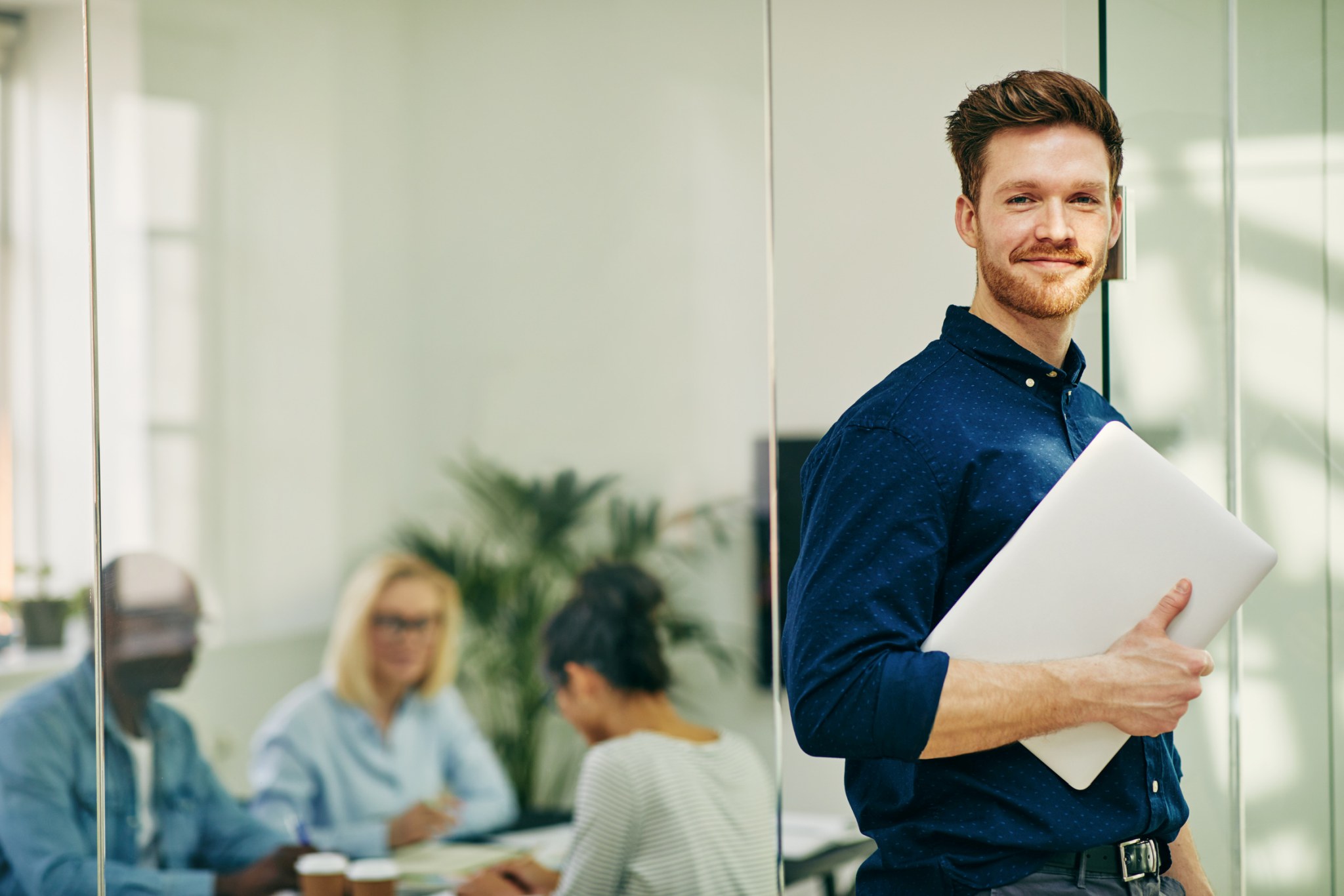 Smiling young businessman standing with his laptop in an office